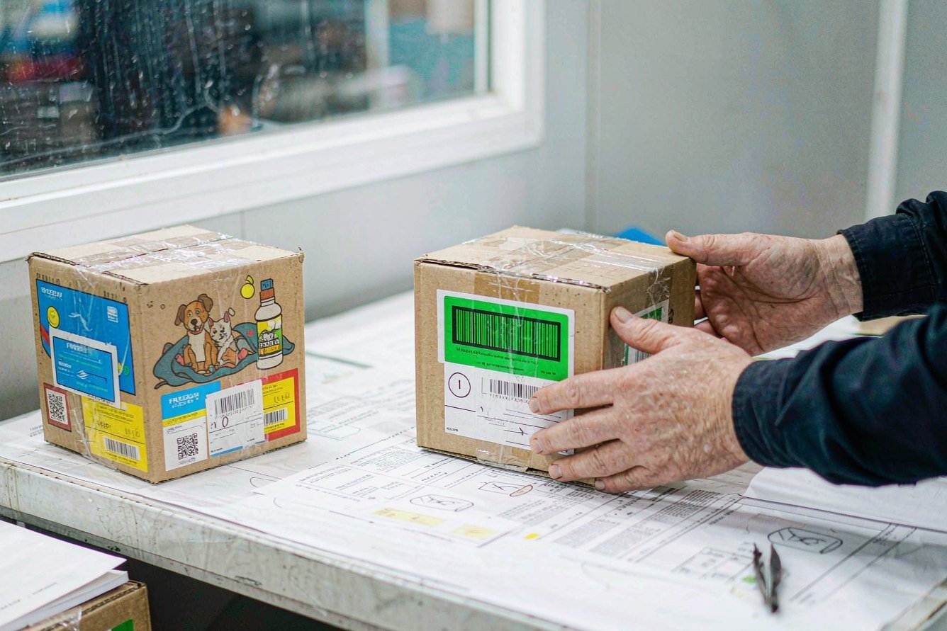 Worker checking retail packaging boxes and barcode labels against a compliance document