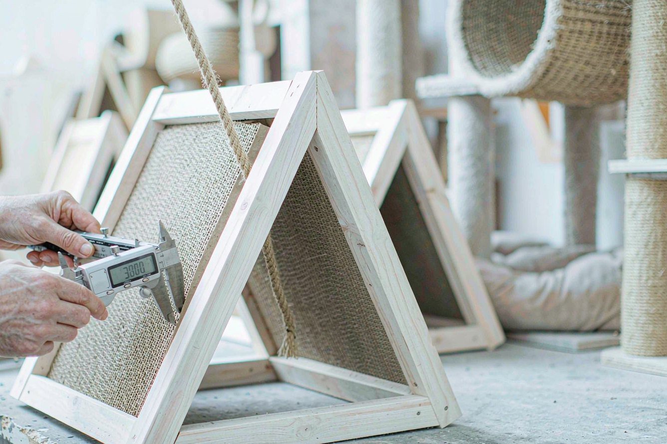 Quality inspector measuring an A-frame cat scratcher house with a digital caliper