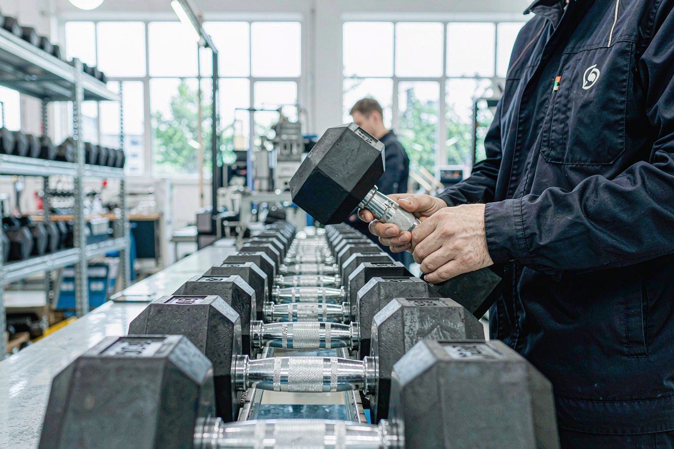 Factory worker inspecting hex rubber dumbbells on the production bench